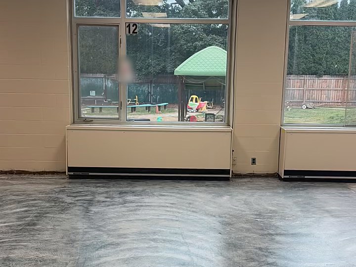 Large commercial room with the old floor skim-coated flat, wall to wall under a row of windows