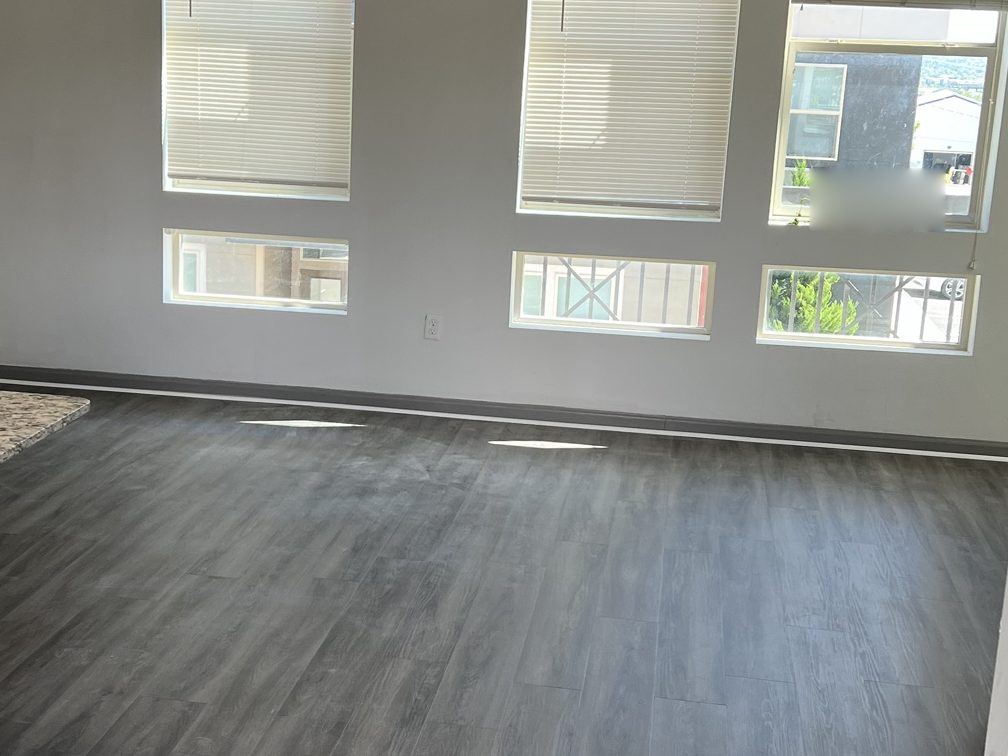 Bright apartment living area finished in grey wood-look LVP under three large windows